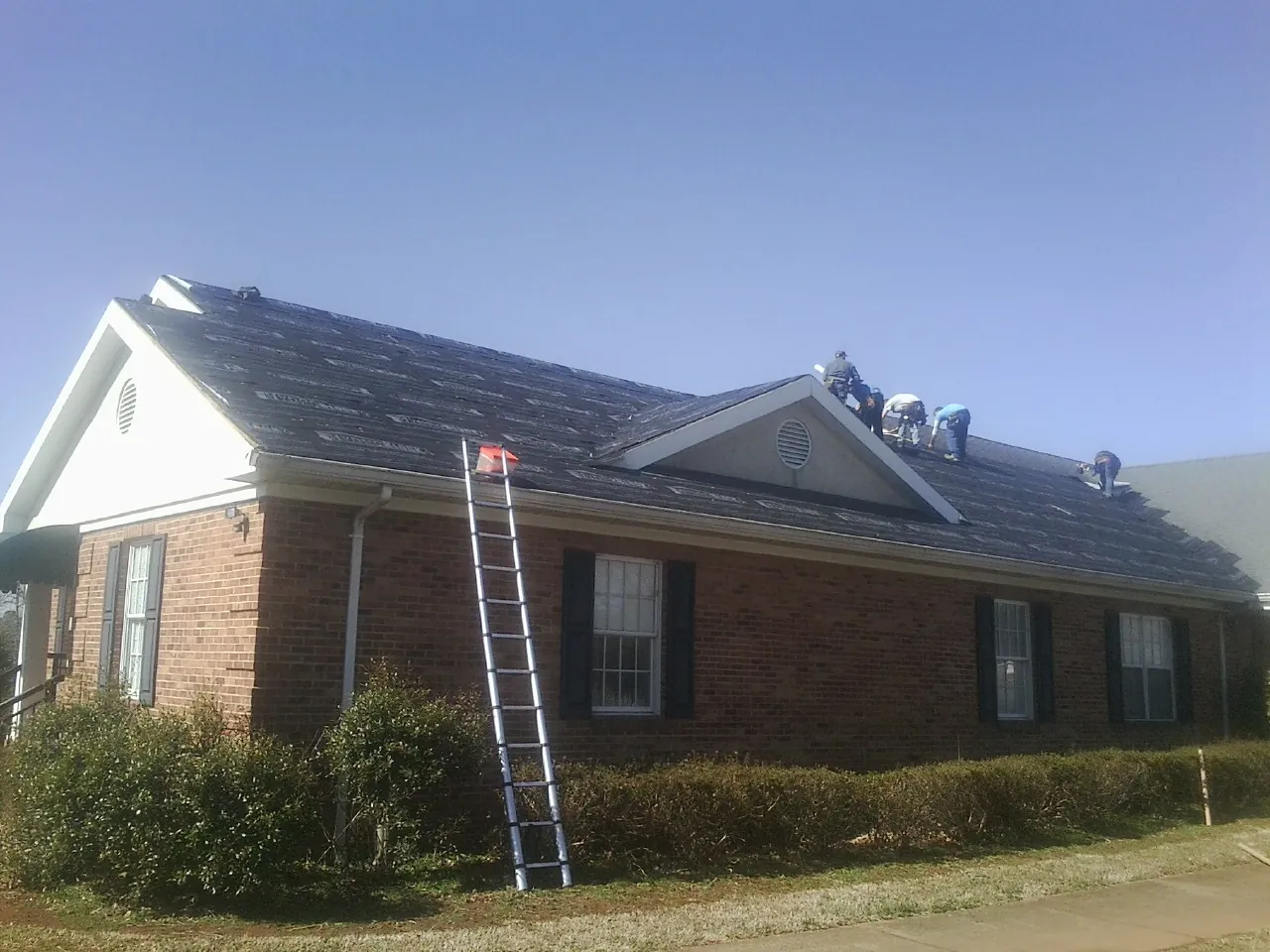 Crew tearing shingles off a brick ranch roof with a ladder set — Emergency Roof Repair work by our crew in Hopkins