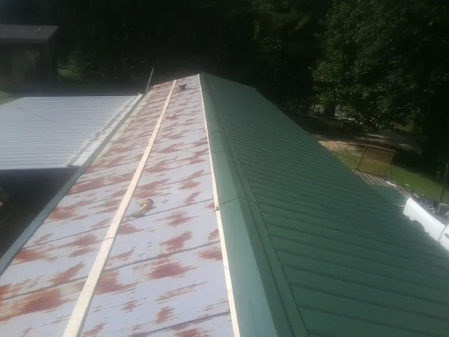 Old rusted panels beside newly installed green metal roofing — Wind Damage Roof Repair by Roofing Brothers in Hopkins